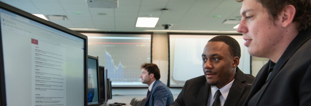 Side view of three young men in suits doing work on computers in a computer lab.